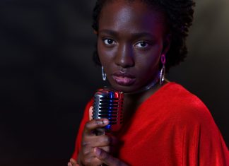 Elegant woman in red with vintage microphone against dark background, conveying emotion.