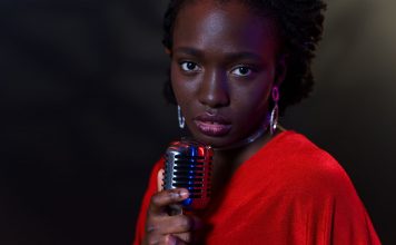 Elegant woman in red with vintage microphone against dark background, conveying emotion.