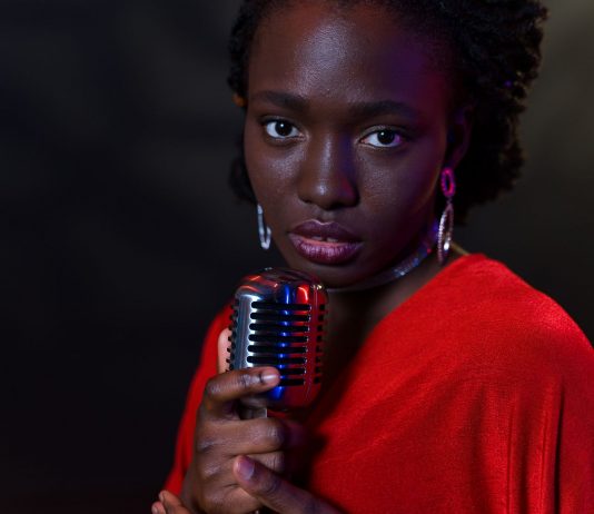 Elegant woman in red with vintage microphone against dark background, conveying emotion.