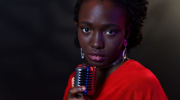Elegant woman in red with vintage microphone against dark background, conveying emotion.