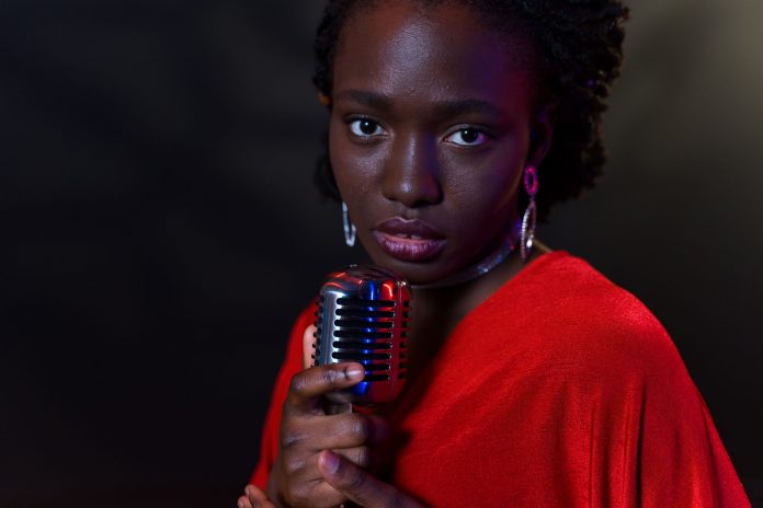Elegant woman in red with vintage microphone against dark background, conveying emotion.