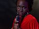 Elegant woman in red with vintage microphone against dark background, conveying emotion.