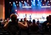 Theater’s Local Value Highlighted in Jersey City Op-Ed A lively concert setting with an engaged audience clapping, under vibrant stage lights.