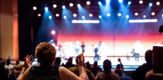 Theater’s Local Value Highlighted in Jersey City Op-Ed A lively concert setting with an engaged audience clapping, under vibrant stage lights.
