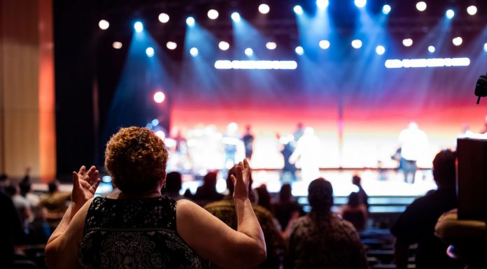 Theater’s Local Value Highlighted in Jersey City Op-Ed A lively concert setting with an engaged audience clapping, under vibrant stage lights.
