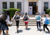 Group of students with backpacks running into school, captured from behind, showing excitement.