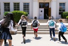 Group of students with backpacks running into school, captured from behind, showing excitement.
