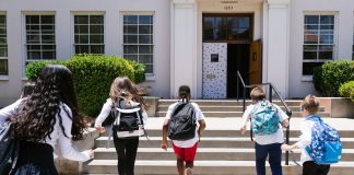 Group of students with backpacks running into school, captured from behind, showing excitement.