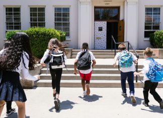 Group of students with backpacks running into school, captured from behind, showing excitement.