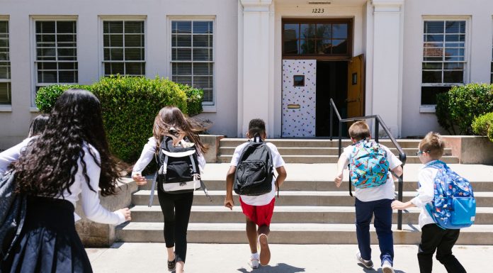 Group of students with backpacks running into school, captured from behind, showing excitement.