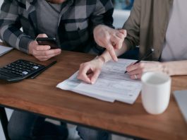 A couple analyzing financial documents and using a calculator at a home table.