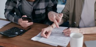 A couple analyzing financial documents and using a calculator at a home table.