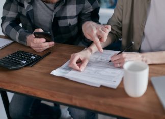 A couple analyzing financial documents and using a calculator at a home table.