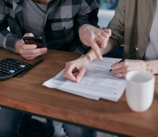 A couple analyzing financial documents and using a calculator at a home table.