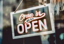 A welcoming 'Come in, We Are Open' sign hanging on a glass window of an urban shop.