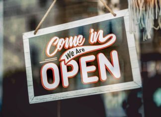 A welcoming 'Come in, We Are Open' sign hanging on a glass window of an urban shop.