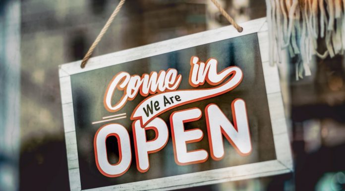 A welcoming 'Come in, We Are Open' sign hanging on a glass window of an urban shop.