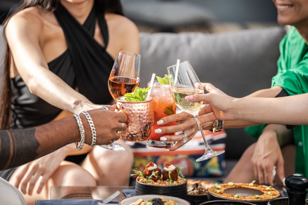 Group of friends clinking glasses with cocktails at an outdoor terrace party in Dubai.