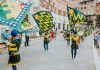 Vibrant street parade with flags and performers in historic square, capturing the lively festival atmosphere.