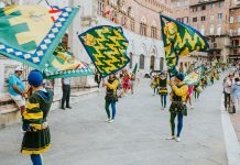 Vibrant street parade with flags and performers in historic square, capturing the lively festival atmosphere.