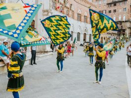 Vibrant street parade with flags and performers in historic square, capturing the lively festival atmosphere.