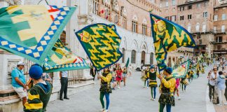 Vibrant street parade with flags and performers in historic square, capturing the lively festival atmosphere.