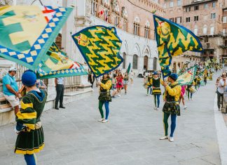 Vibrant street parade with flags and performers in historic square, capturing the lively festival atmosphere.
