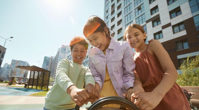 Diverse group of children laughing and playing outdoors in a city playground.