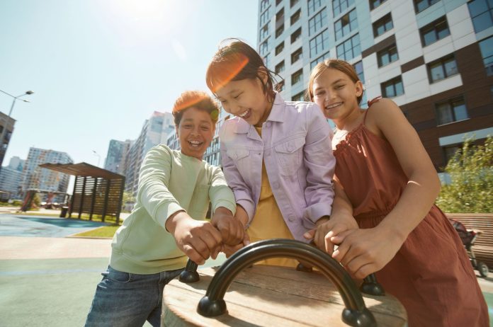 Diverse group of children laughing and playing outdoors in a city playground.