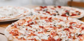 Close-up of freshly baked pizzas with mushrooms served on a wooden table.