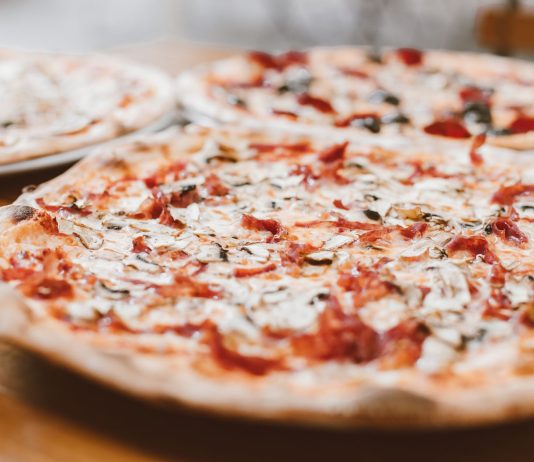 Close-up of freshly baked pizzas with mushrooms served on a wooden table.