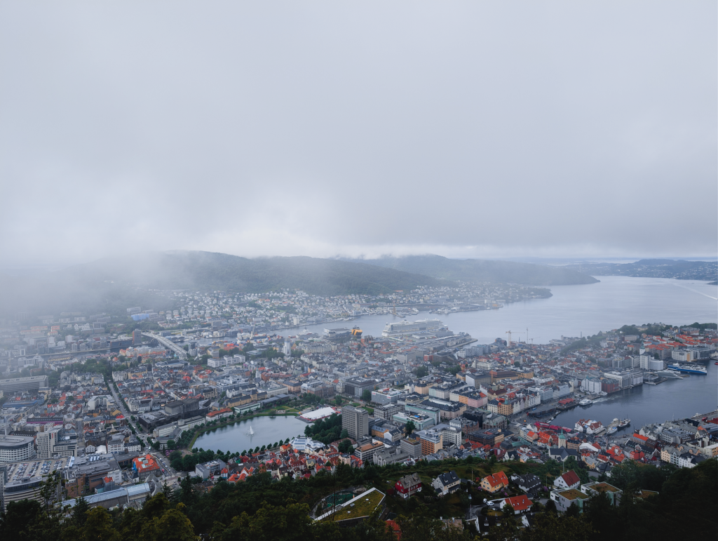 Aerial view of Bergen, Norway, with its harbor and surrounding hills on a cloudy day.