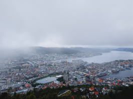 Aerial view of Bergen, Norway, with its harbor and surrounding hills on a cloudy day.