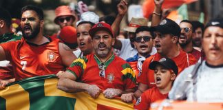 Group of diverse soccer fans cheering passionately, waving flags and celebrating in a vibrant parade.