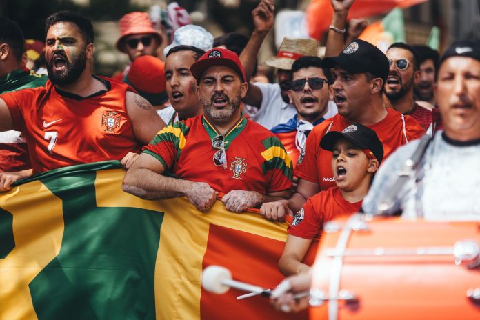 Group of diverse soccer fans cheering passionately, waving flags and celebrating in a vibrant parade.