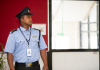 Security guard in uniform standing alert at a building entrance.