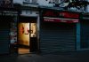 A closed café with a partially open door revealing dim interior lighting, creating a mysterious street scene.