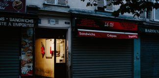 A closed café with a partially open door revealing dim interior lighting, creating a mysterious street scene.