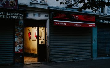 A closed café with a partially open door revealing dim interior lighting, creating a mysterious street scene.