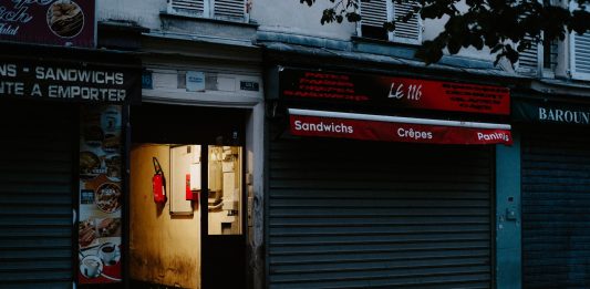A closed café with a partially open door revealing dim interior lighting, creating a mysterious street scene.