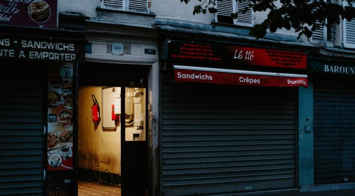 A closed café with a partially open door revealing dim interior lighting, creating a mysterious street scene.