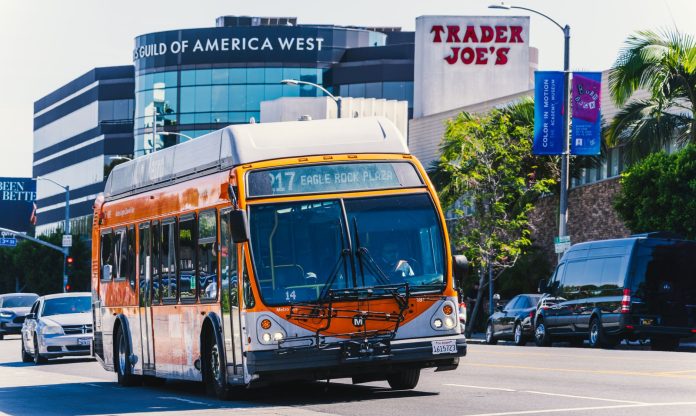 Metro bus on Eagle Rock Plaza route in Los Angeles, passing iconic Trader Joe's on a sunny day.
