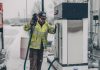 A man wearing a jacket refuels a truck at a gas station during winter with snow falling.