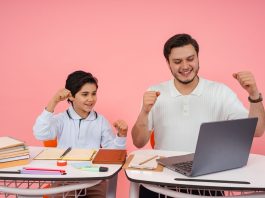 Father and son joyfully celebrate finishing homework together on a laptop.