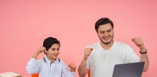 Father and son joyfully celebrate finishing homework together on a laptop.