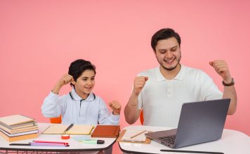 Father and son joyfully celebrate finishing homework together on a laptop.