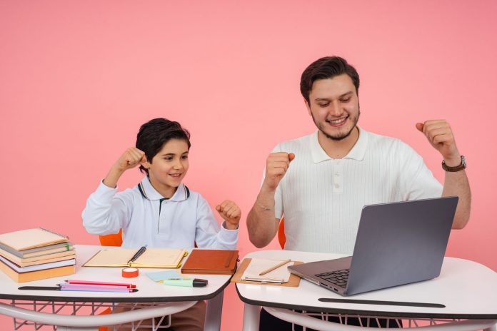high-tech-senior-named-national-merit-semifinalist Father and son joyfully celebrate finishing homework together on a laptop.