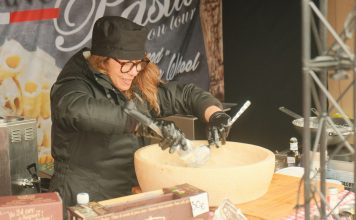 Hoboken Italian Festival Celebrates 100 Years With Local Eateries Female chef preparing pasta in a large parmesan wheel at an outdoor food stall, showcasing culinary techniques.