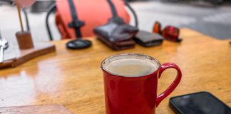 A cozy café setup with a red coffee mug and smartphone on a wooden table.