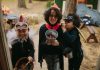 Three children in Halloween costumes joyfully trick-or-treating with candy buckets.